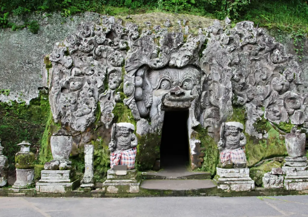 Ancient stone entrance of Goa Gajah temple near Ubud featuring intricate Balinese carvings, moss-covered statues, and a historic cave sanctuary.